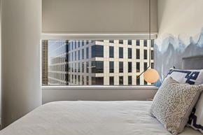 Dallas apartment for rent - A bedroom with a large bed and a window with a view of a cityscape.