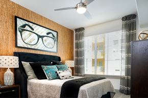 Austin apartment for rent - A bedroom with a bed, pillows, a ceiling fan, and a picture of glasses on the wall.