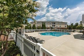 High Point apartment for rent - A pool surrounded by a white fence with trees in the foreground.