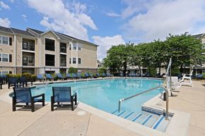 Mt Laurel apartment for rent - A swimming pool surrounded by chairs and trees in front of a building.