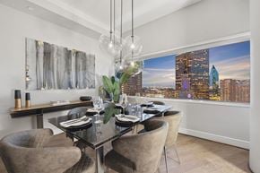 Dallas apartment for rent - A modern dining room with a glass table and chairs, a chandelier, and a cityscape view.