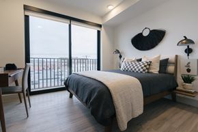 North Kansas City apartment for rent - Two-Bedroom Apartments in North Kansas City, MO - The OxBow - Spacious Bedroom with High Ceiling, Luxury Vinyl Flooring, Bed, Nightstands with Lamps, Wall Art, and Window with Energy Efficient Roller Shade
