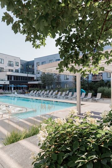 Kansas City apartment for rent - A pool surrounded by chairs and trees with a building in the background.
