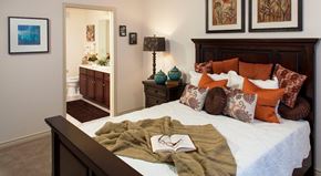 Fort Worth apartment for rent - A bedroom with a bed, a lamp, a mirror, and a painting on the wall.