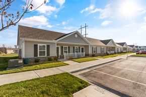 Belton apartment for rent -  Dog-Friendly Senior Townhomes in Belton, MO - Traditions Villas 55+ - An Off-Street Parking Area Fronting a Row of Houses with Fences and Yards.