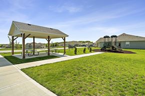 Blue Springs apartment for rent - Townhomes In Blue Springs, MO - Chapman Ridge Townhomes - A Park With Concrete Walkways, Picnic Tables, Playground Area, Lush Green Lawn, And Clear Blue Sky.