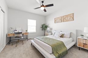 Raymore apartment for rent - Dog-Friendly townhomes in Raymore, MO - Ascend - Spacious Bedroom With Large Bed, Nightstands With Lamps, Ceiling Fan, Plush Carpet, Work Desk, And Large Window.