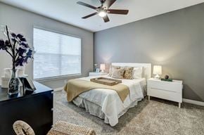 Dallas apartment for rent - A bedroom with a white bed and a ceiling fan.