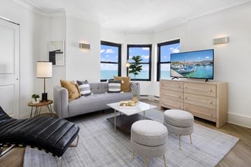Chicago apartment for rent - A modern living room with a grey sofa, a black leather chair, a white coffee table, and a television displaying a coastal scene.