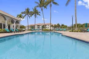 Delray Beach apartment for rent - a large swimming pool with palm trees in front of a building