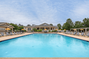 Knightdale apartment for rent - A large swimming pool in front of a building with lounge chairs on either side.