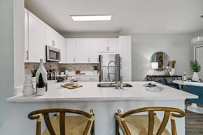 Saraland apartment for rent - A kitchen with white cabinets and a white countertop with two chairs in front of it.