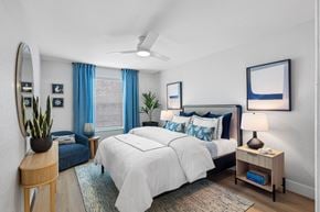 Boca Raton apartment for rent - A bedroom with a large bed, a side table with a lamp, and a mirror on the wall.