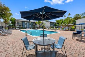 Tamarac apartment for rent - A spacious pool area with a table, chairs and an umbrella overlooking a pool.