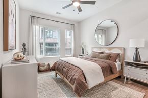 Atlanta apartment for rent - A bedroom with a large bed, a ceiling fan, and a round mirror on the wall.