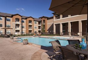 Fort Worth apartment for rent - A pool area with chairs and umbrellas in front of apartment buildings.
