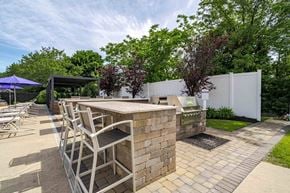 Medford apartment for rent - A patio with a bar and chairs is surrounded by a white fence and greenery.
