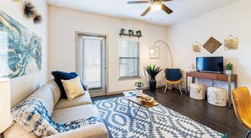 San Antonio apartment for rent - A living room with a beige couch, a blue and white patterned rug, a wooden chair, and a television on a wooden stand.