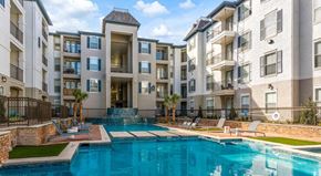 Dallas apartment for rent - A large swimming pool is surrounded by lounge chairs in front of apartment buildings.