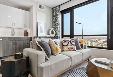 Skokie apartment for rent - A modern living room with a grey couch and a large window overlooking a cityscape.