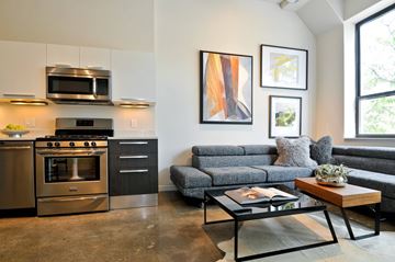 Chicago apartment for rent - A modern kitchen with a stainless steel oven and microwave, a grey sofa, and a coffee table with a book on it.