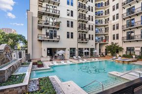 Dallas apartment for rent - A large swimming pool surrounded by a stone wall and a patio area with chairs and umbrellas.