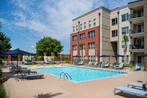 Columbia apartment for rent - A swimming pool surrounded by lounge chairs and umbrellas in front of a multi-story building.