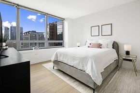 Chicago apartment for rent - A bedroom with a large bed and a city view through the window.