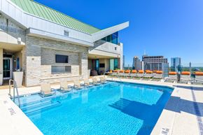 Atlanta apartment for rent - A swimming pool is surrounded by chairs and a building with a green roof is in the background.