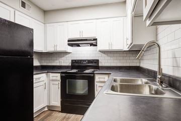 Taylors apartment for rent - A black refrigerator sits next to a stove in a kitchen with white cabinets.