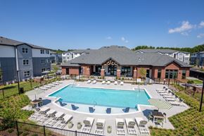 Gainesville apartment for rent - A large swimming pool surrounded by lounge chairs and a building in the background.