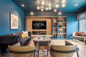 Nashville apartment for rent - A living room with a black couch, a coffee table, and a bookshelf with the word LOCAL on it.
