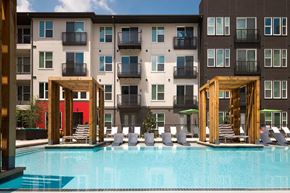 Dallas apartment for rent - A pool area with lounge chairs and wooden structures in front of apartment buildings.