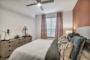 Round Rock apartment for rent - A bedroom with a bed, pillows, a ceiling fan, and a dresser with decorative items.