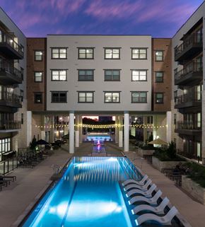 Dallas apartment for rent - A swimming pool in front of a building with lights on.