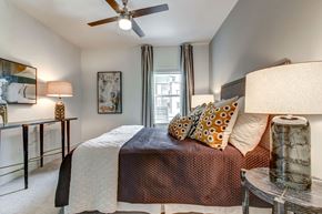 Dallas apartment for rent - A bedroom with a bed, a ceiling fan, and a nightstand with a lamp.