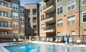 Dallas apartment for rent - A swimming pool is surrounded by lounge chairs in front of apartment buildings.