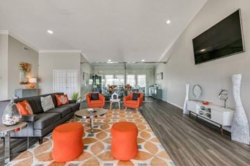 Lafayette apartment for rent - A living room with a grey couch, orange ottoman, and a television mounted on the wall.