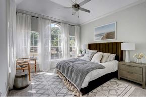 Dallas apartment for rent - A bedroom with a large bed, a ceiling fan, and a view of the outdoors through the window.