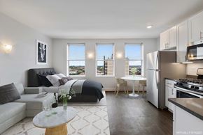 Chicago apartment for rent - A modern living room with a grey couch, a coffee table, and a kitchen area with stainless steel appliances.