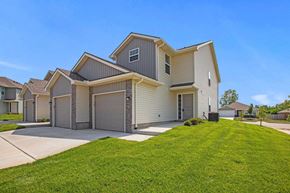 Spring Hill apartment for rent - Gardner KS Pet-Friendly Apartments - Oak Woods Townhomes - A Two-Story House With Attached Garages, A Manicured Lawn, And A Clear Blue Sky.