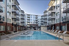 Huntsville apartment for rent - A swimming pool is surrounded by lounge chairs in front of apartment buildings.