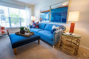 New Bern apartment for rent - A living room with a blue couch, a wooden coffee table, and a glass side table with a lamp.