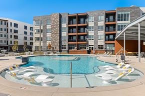 Kansas City apartment for rent - 2-Bedroom Apartments in Brookside, Kansas City, MO - Brookside Commons - Resort-Style Swimming Pool With In-Water Lounge Chairs, Sundeck Seating, and Modern Apartment Buildings.