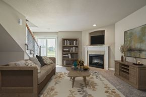 Peculiar apartment for rent - Two-Bedroom Townhomes in Peculiar, MO - Bradley’s Crossing - Living Room with Carpet Flooring, Long Couch, Coffee Table, Media Console, Large Painting, Fireplace, Mounted TV, and a Bookshelf.