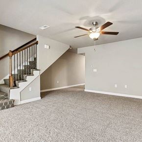 Belton apartment for rent - 3-Bedroom Townhomes in Belton, MO - Traditions Townhomes - A Spacious Empty Room with Carpet Flooring, Ceiling Fan with Light, and a Carpeted Staircase.