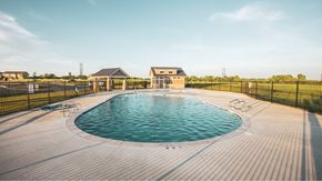Belton apartment for rent - Pet-Friendly Townhomes in Belton, MO - Traditions Townhomes - An Outdoor Swimming Pool Surrounded by a Deck, Blank Fence, and Landscaping, Overlooking a Pavilion and the Clubhouse.