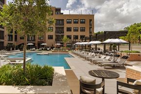 Dallas apartment for rent - A pool area with chairs and umbrellas in front of a building.