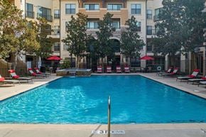Rockwall apartment for rent - A swimming pool in front of a building with red umbrellas and lounge chairs.