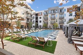 Dallas apartment for rent - A pool surrounded by chairs and trees in front of apartment buildings.